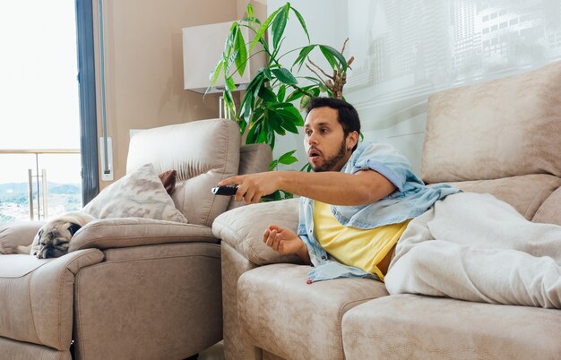 Foto de um belo homem hispânico deitado em um sofá e assistindo TV