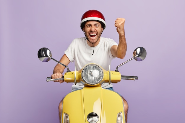 Foto de um cara confiante com capacete dirigindo uma scooter amarela