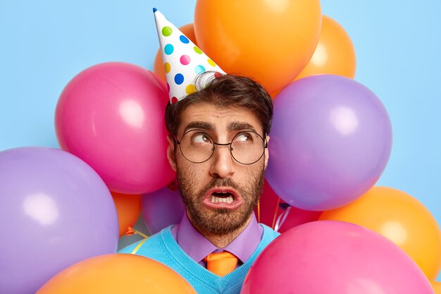 Foto de um cara infeliz rodeado de balões de festa posando