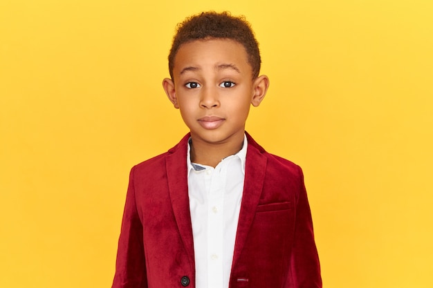 Foto grátis foto de um garotinho afro-americano charmoso e fofo, vestindo roupas elegantes, posando isolado, olhando para a câmera fascinado, surpreso com os preços de venda altos