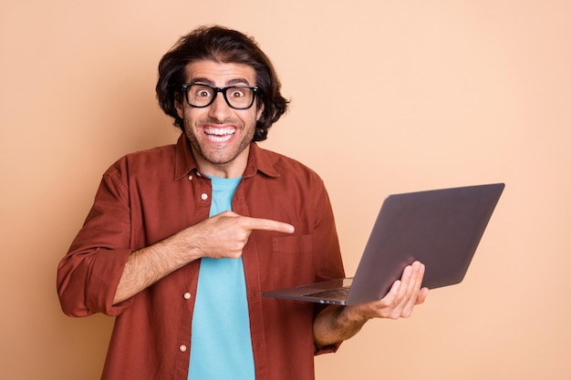 Foto de um homem animado apontando o dedo para um laptop segurando uma das mãos, isolado em um fundo de cor bege pastel