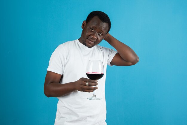 Foto de um homem de camiseta branca segurando uma taça de vinho contra a parede azul