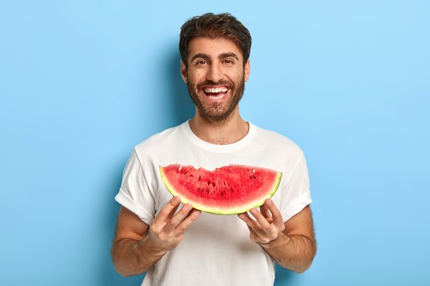 Foto de um homem sorridente em um dia de verão segurando uma fatia de melancia pela cintura