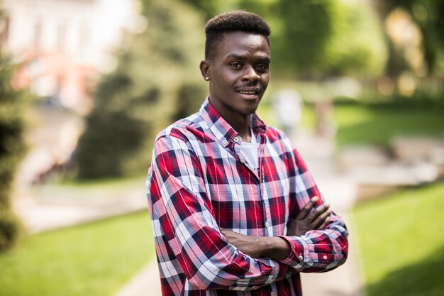 Foto de um jovem africano andando na rua em pé com os braços cruzados.