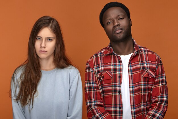 Foto de um jovem casal com olhares tristes e infelizes depois de uma noite sem dormir por causa de seu filho bebê chorando, posando isolado em. Amor, relacionamento e conceito de união inter-racial