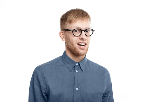 Foto de um jovem emocional engraçado com a barba por fazer usando óculos elegantes, abrindo a boca em espanto, sendo chocado com uma notícia inesperada, olhando em total descrença. Choque e surpresa