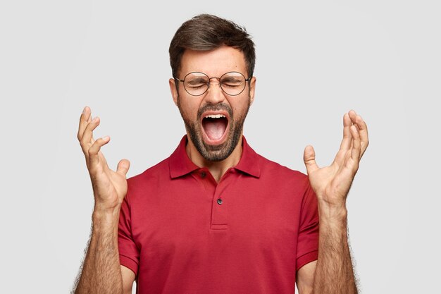 Foto de um jovem louco com a barba por fazer gesticula com raiva e exclama em negatividade