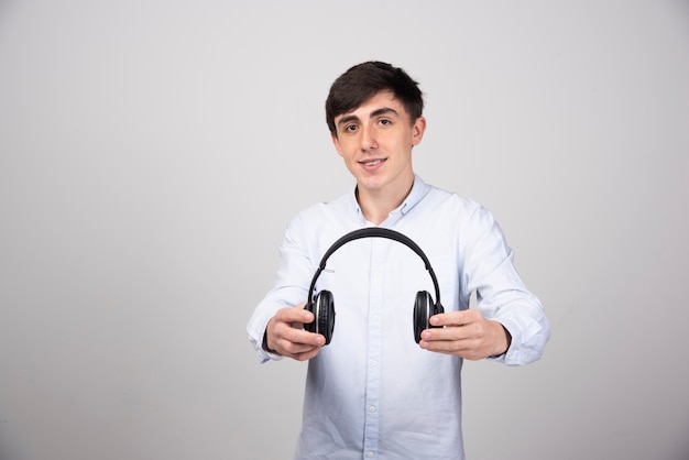 Foto de um modelo de cara jovem segurando fones de ouvido sem fio e olhando para a câmera
