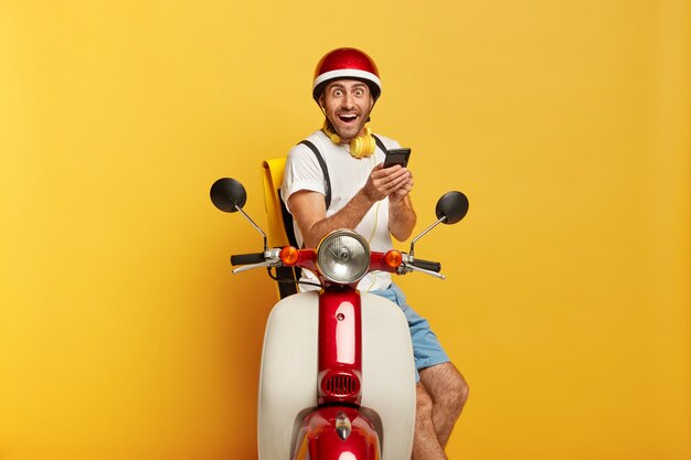 Foto de um motorista masculino bonito e feliz em uma scooter com capacete vermelho