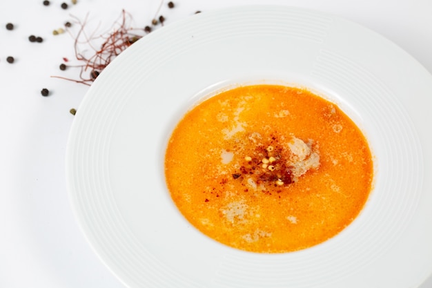 Foto de um prato de sopa com sopa tripla em uma mesa branca decorada com bolas de pimenta preta