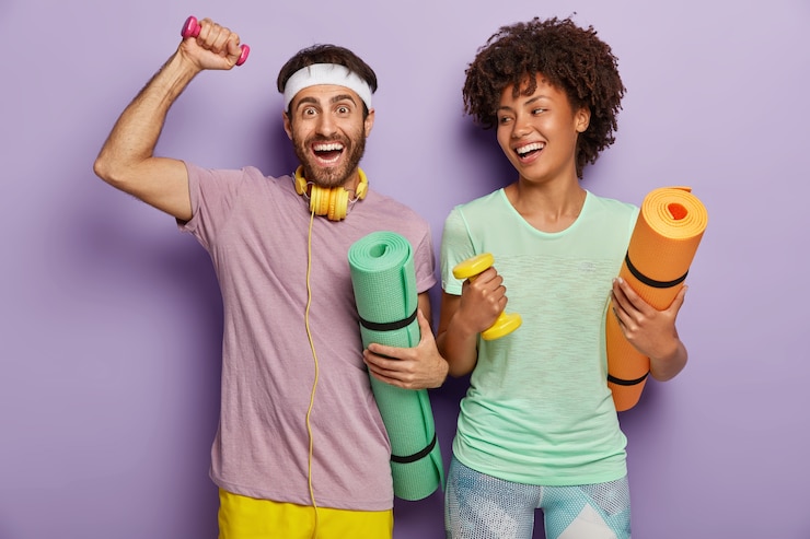 Foto grátis foto de um rapaz e uma mulher felizes trabalhando no bíceps com pesos, carregando karemats, tendo expressões alegres, treinando juntos, vestidos com roupas casuais, motivados para um estilo de vida saudável e esporte