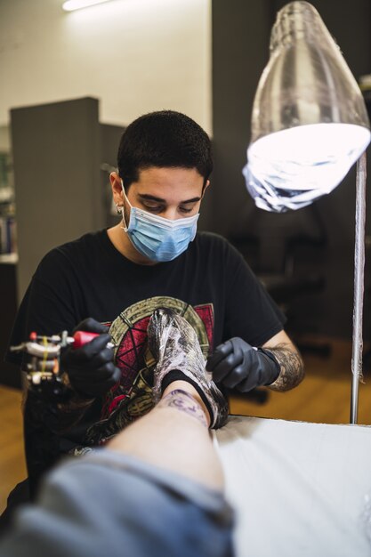 Foto de um tatuador tatuando a perna de seu cliente