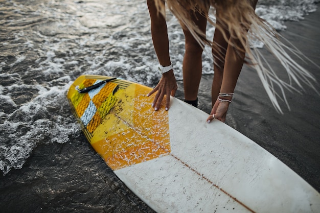 Foto de uma garota de cabelo comprido colocando uma prancha de surf na água do mar