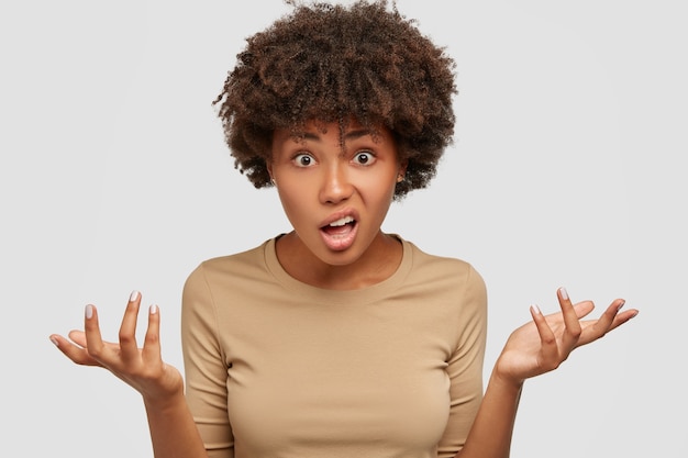 Foto de uma jovem confusa e hesitante com um penteado afro encaracolado, dando de ombros