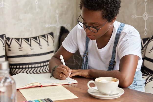 Foto de uma jovem empresária profissional negra autônoma que escreve boas ideias para desenvolver seu negócio em um caderno