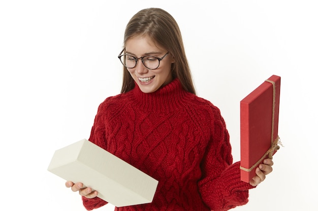 Foto de uma jovem linda em êxtase usando óculos e um suéter aconchegante abrindo uma caixa de presente