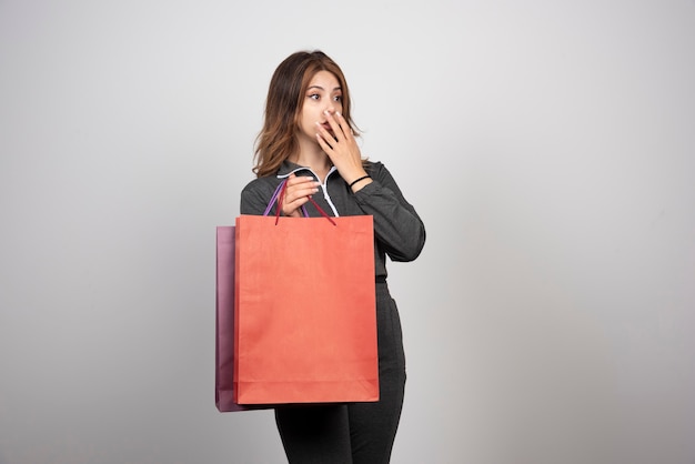 Foto de uma jovem mulher com sacolas de compras e acenando com a mão.