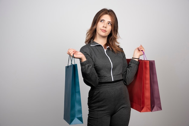 Foto de uma jovem mulher pensativa segurando sacolas de compras.