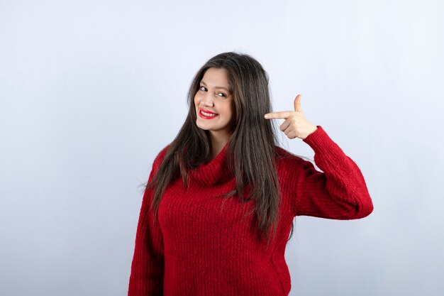 Foto de uma jovem sorridente com um suéter vermelho apontando para longe