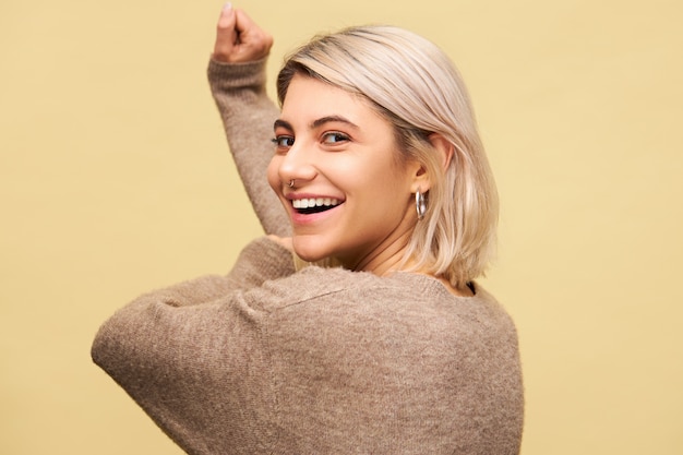 Foto de uma linda garota alegre com um sorriso radiante encantador posando virando a cabeça, movendo as mãos como se dançando ao som de uma música agradável e agradável. conceito de pessoas, estilo de vida, alegria e emoções positivas