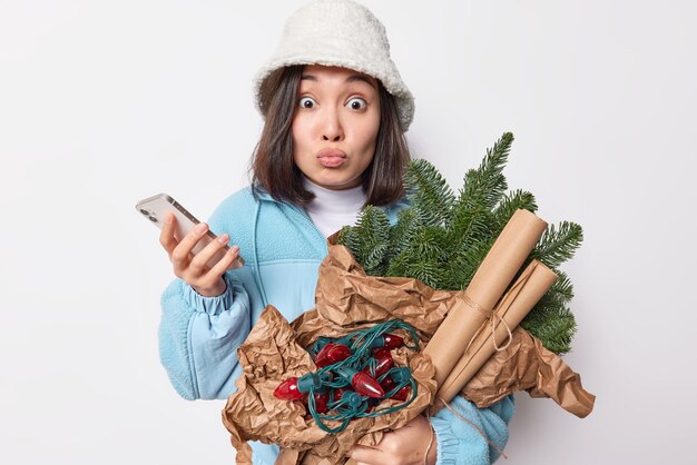 Foto de uma linda mulher asiática impressionada encara olhos esbugalhados tem lábios arredondados reage a algo chocante se prepara para as próximas férias vestida com roupas de inverno mantém smartphone espera por chamada