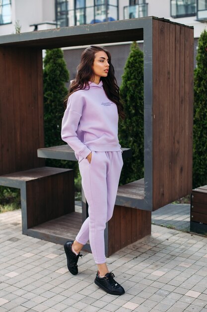 Foto de uma linda mulher caucasiana em um terno esporte roxo e tênis preto mantém as mãos nos bolsos