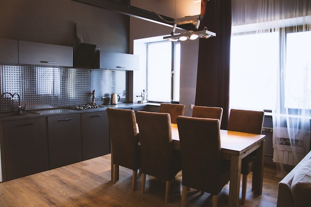 Foto de uma mesa de madeira com cadeiras de madeira perto das cortinas da janela em uma cozinha com interior preto
