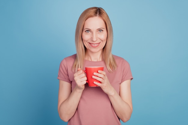 Foto de uma mulher alegre positiva e muito doce segurando uma caneca de café sorrindo isolada sobre um fundo de cor azul