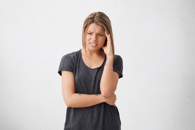 Foto de uma mulher exausta e preocupada com um olhar triste e abatido, o rosto carrancudo, segurando a mão na têmpora, indo chorar tendo muitos problemas sem saber como resolvê-los. pessoas, estresse e problemas