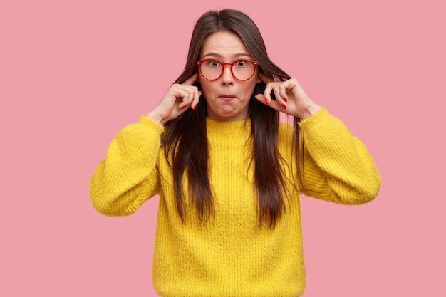 Foto de uma senhora surpresa que não suporta um som terrível, surpreendida com boatos, entope os ouvidos e usa roupas amarelas