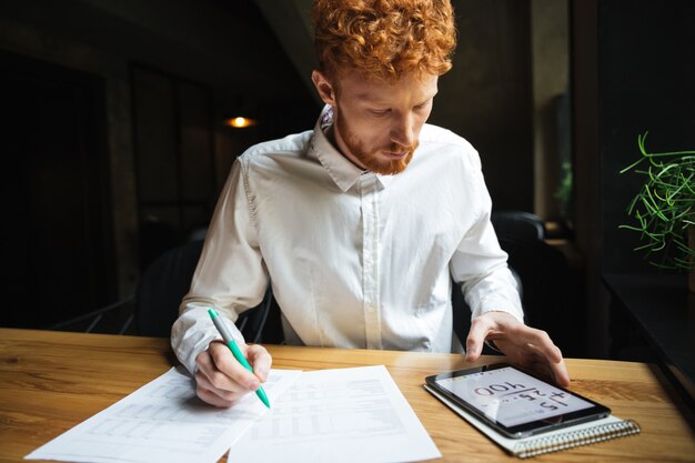 Foto do freelancer sério jovem readhead trabalhando em casa