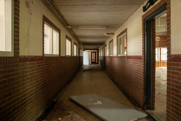 Foto do interior de um corredor vazio de uma escola abandonada com portas quebradas