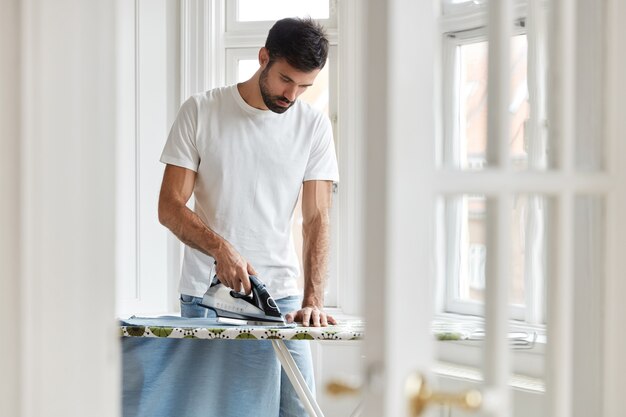 Foto do marido responsável ou solteiro ocupado com o trabalho doméstico passando a camisa pela manhã na mesa antes do trabalho