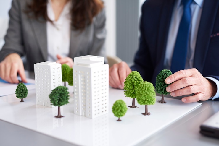 Na imagem, um homem e uma mulher estão organizando uma maquete de um futuro condomínio de prédios já pensando no Licenciamento Ambiental. Na maquete, algumas árvores estão sendo colocadas. | Fonte: Freepik