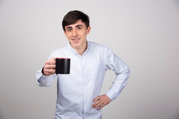 Foto do retrato de um modelo sorridente de pé e oferecendo um copo de bebida