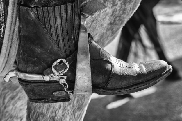 Foto em escala de cinza de pés em botas no estribo de uma sela