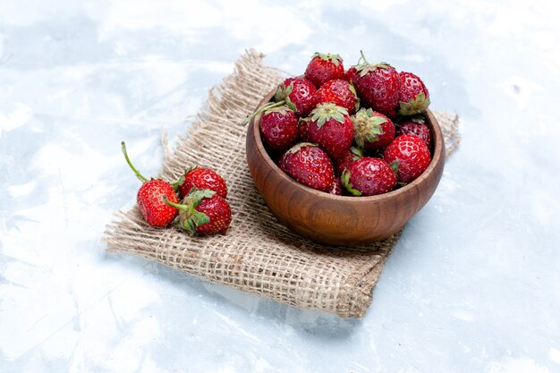 Foto frontal de morangos vermelhos frescos dentro de um pote marrom em uma mesa branca clara com sabor de vitamina fresca