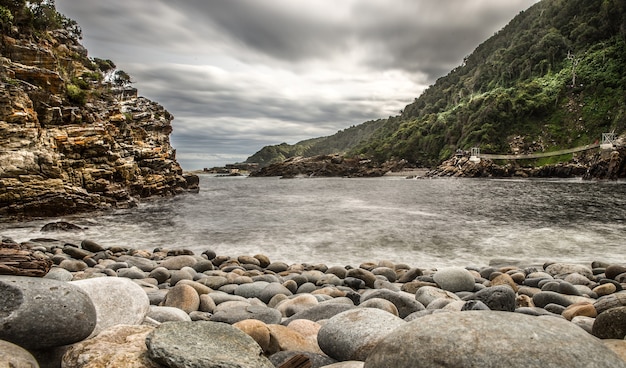 Foto grande angular da praia ao redor das montanhas sob um céu nublado