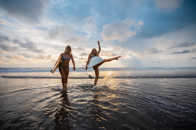 Foto grande angular de duas mulheres em pé na praia durante o pôr do sol