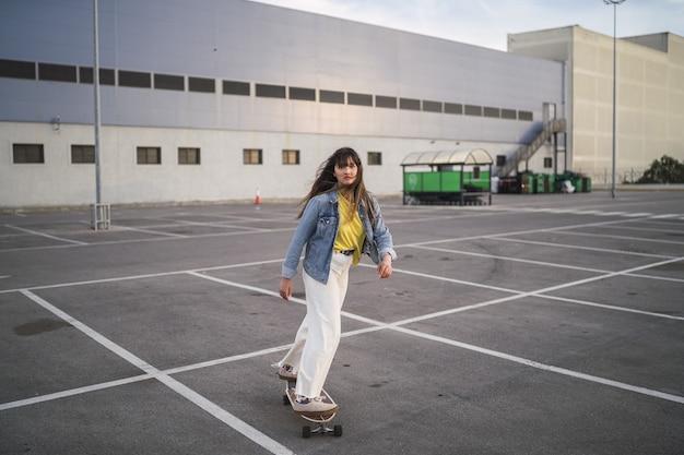 Foto grande angular de uma garota em um skate atrás de um prédio