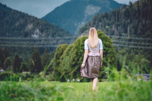 Foto grande angular de uma mulher de saia e gravata caminhando em direção às montanhas