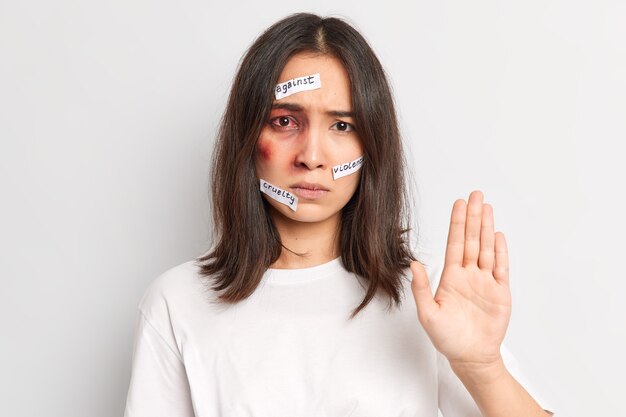 Foto horizontal de mulher asiática ypung fazendo gesto de pare e pedindo para parar de machucá-la torna-se vítima de agressão sexual com a pele machucada vestida com uma camiseta casual