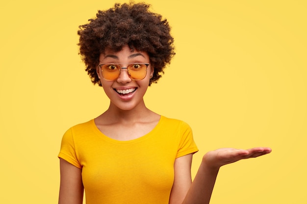 Foto horizontal de mulher negra feliz com tons da moda, cabelo crespo, vestida com roupas casuais, com espaço de cópia