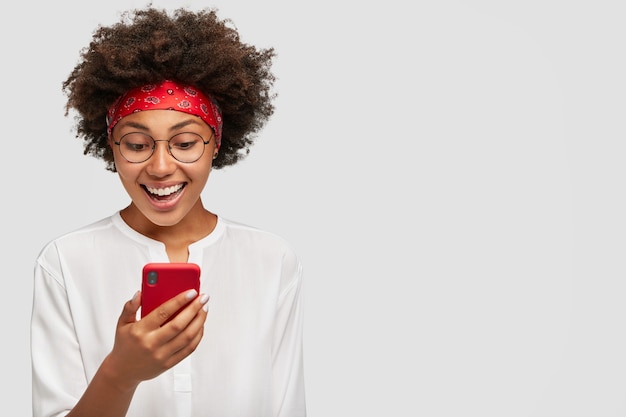 Foto horizontal de um adulto negro de aparência agradável, animado com o bate-papo por vídeo, carregando um celular moderno, com um sorriso largo