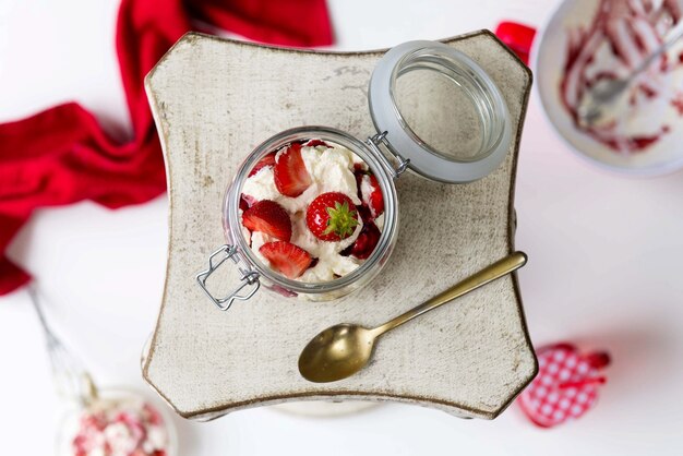 Foto horizontal de um pote de morangos e creme branco servido em um prato quadrado com uma colher