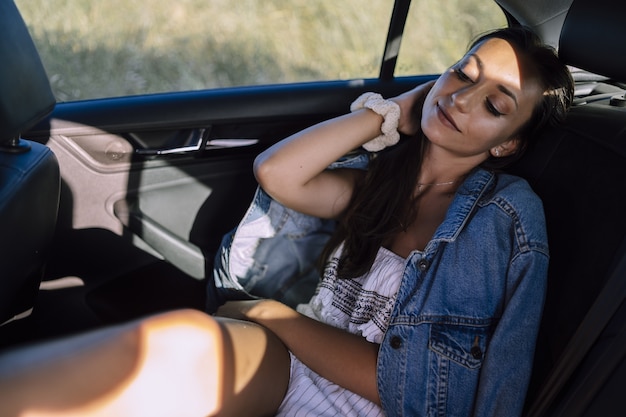 Foto horizontal de uma bela jovem caucasiana posando no banco de trás de um carro em um campo