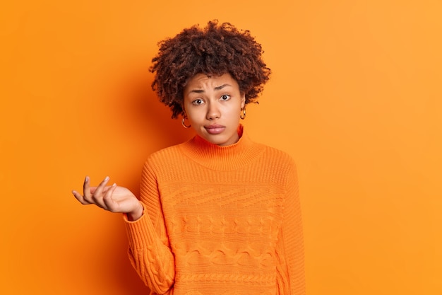 Foto horizontal de uma jovem afro-americana confusa e hesitante, encolhendo os ombros e parecendo perplexa e duvidosa, parece insegura