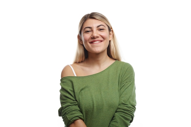 Foto horizontal de uma jovem estudante europeia positiva com piercing no nariz e cabelo tingido posando, olhando com um sorriso encantador e feliz, sentindo-se relaxada após as aulas na universidade