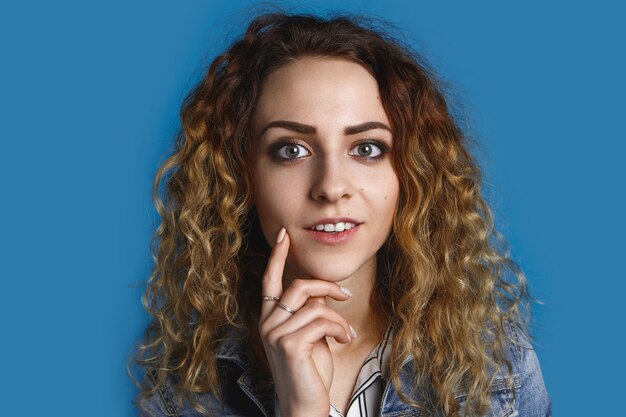 Foto grátis foto horizontal de uma jovem europeia atraente de olhos verdes, vestida elegantemente, segurando a mão sob o queixo com um misterioso sorriso pensativo como se tivesse uma ótima ideia