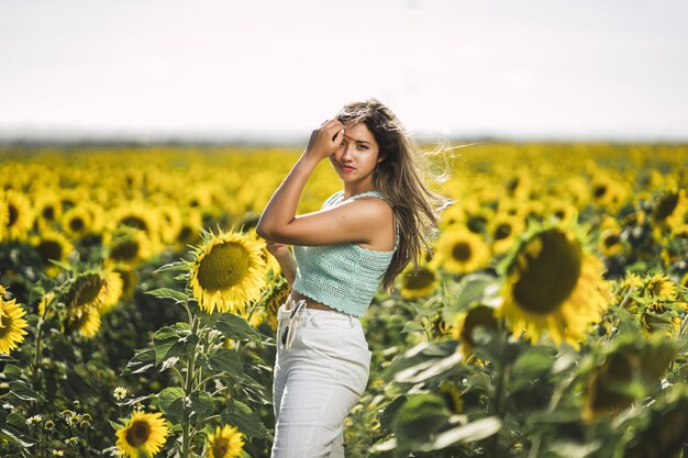 Foto horizontal de uma jovem mulher branca posando em um campo brilhante de girassóis em um dia ensolarado